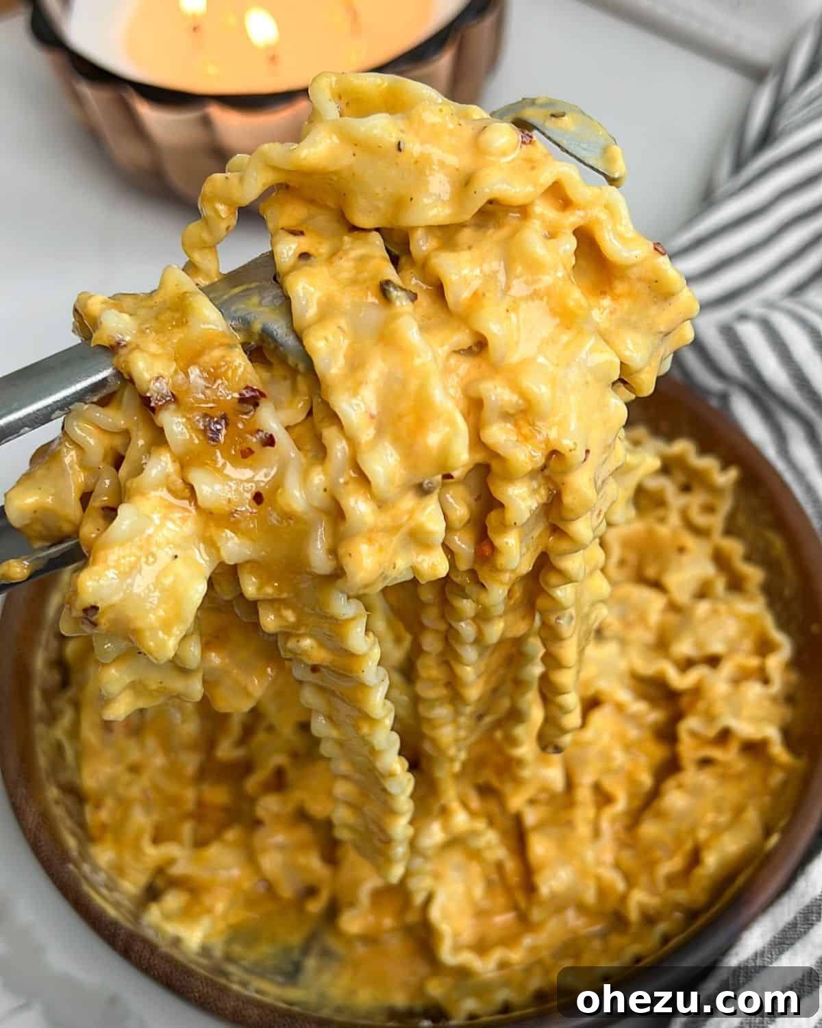 Fork lifting creamy pumpkin alfredo pasta from a bowl, garnished with herbs