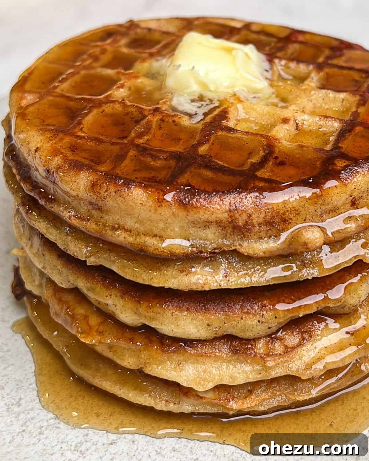 A vibrant close-up of a perfectly cooked stack of French toast waffles, richly topped with butter and dripping with golden maple syrup, emphasizing their irresistible texture and appeal.
