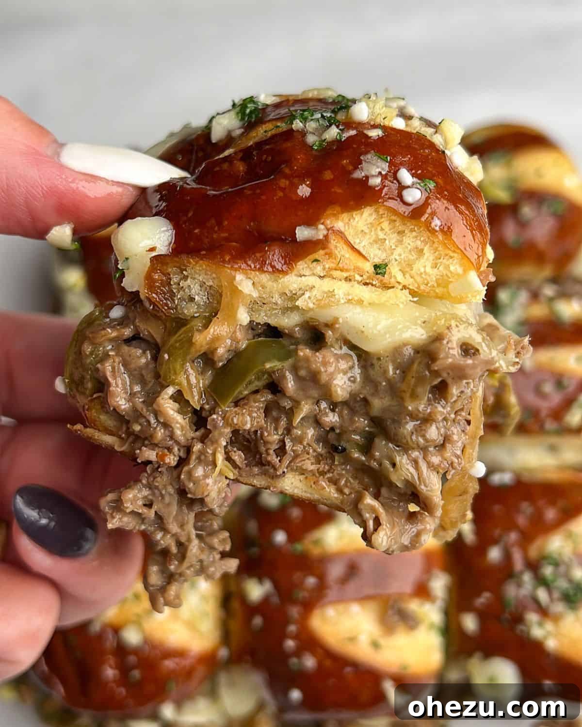 A hand holding a perfectly assembled Philly cheesesteak slider, showcasing the melted cheese and juicy filling.