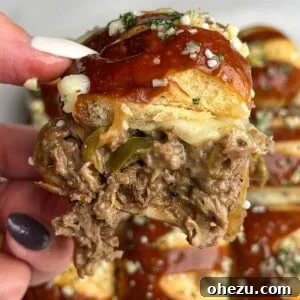 A hand holding a Philly cheesesteak slider up to the camera.