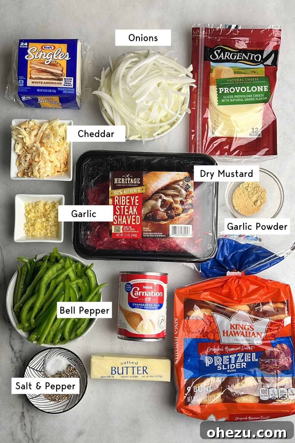 A perfectly arranged flat lay of key ingredients required for making Philly cheesesteak sliders, including ribeye, onions, peppers, cheese, and buns.