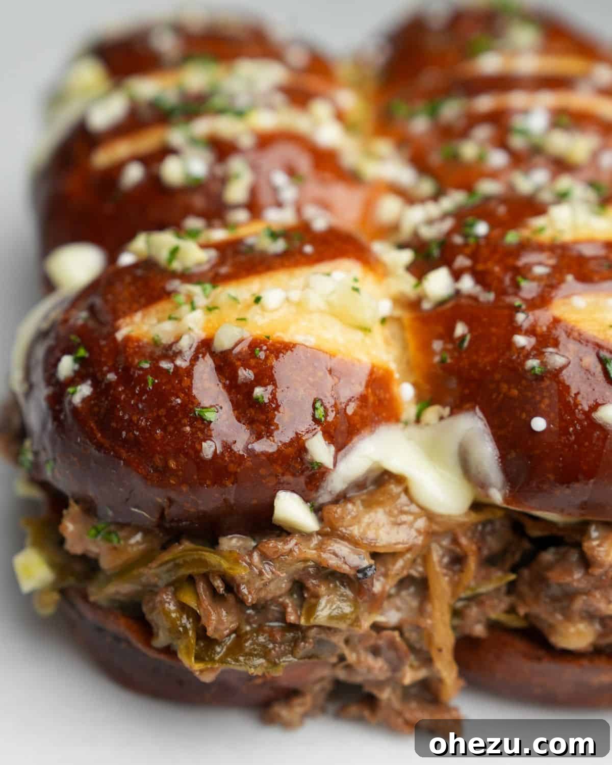 A close-up image of a perfectly golden Philly cheesesteak slider brushed with glistening garlic butter, ready to be served.