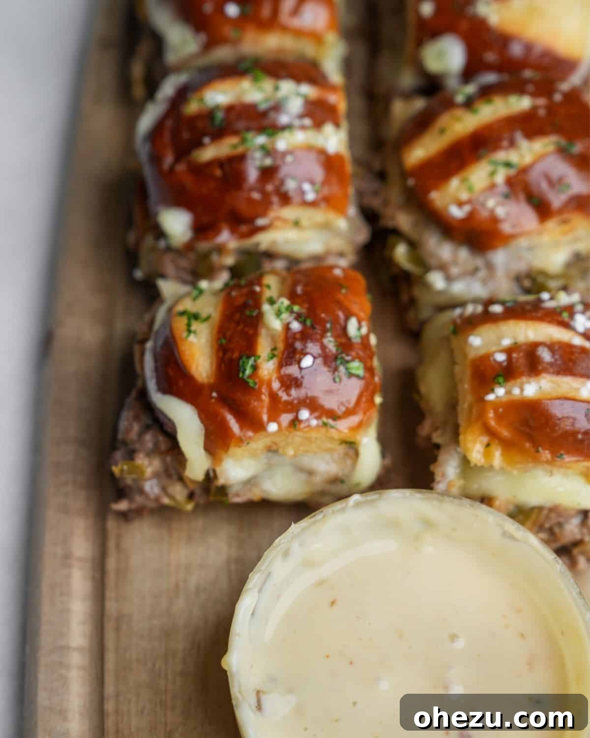 A mouth-watering close-up of a Philly cheesesteak slider, highlighting the rich cheese whiz and savory garlic butter on top.