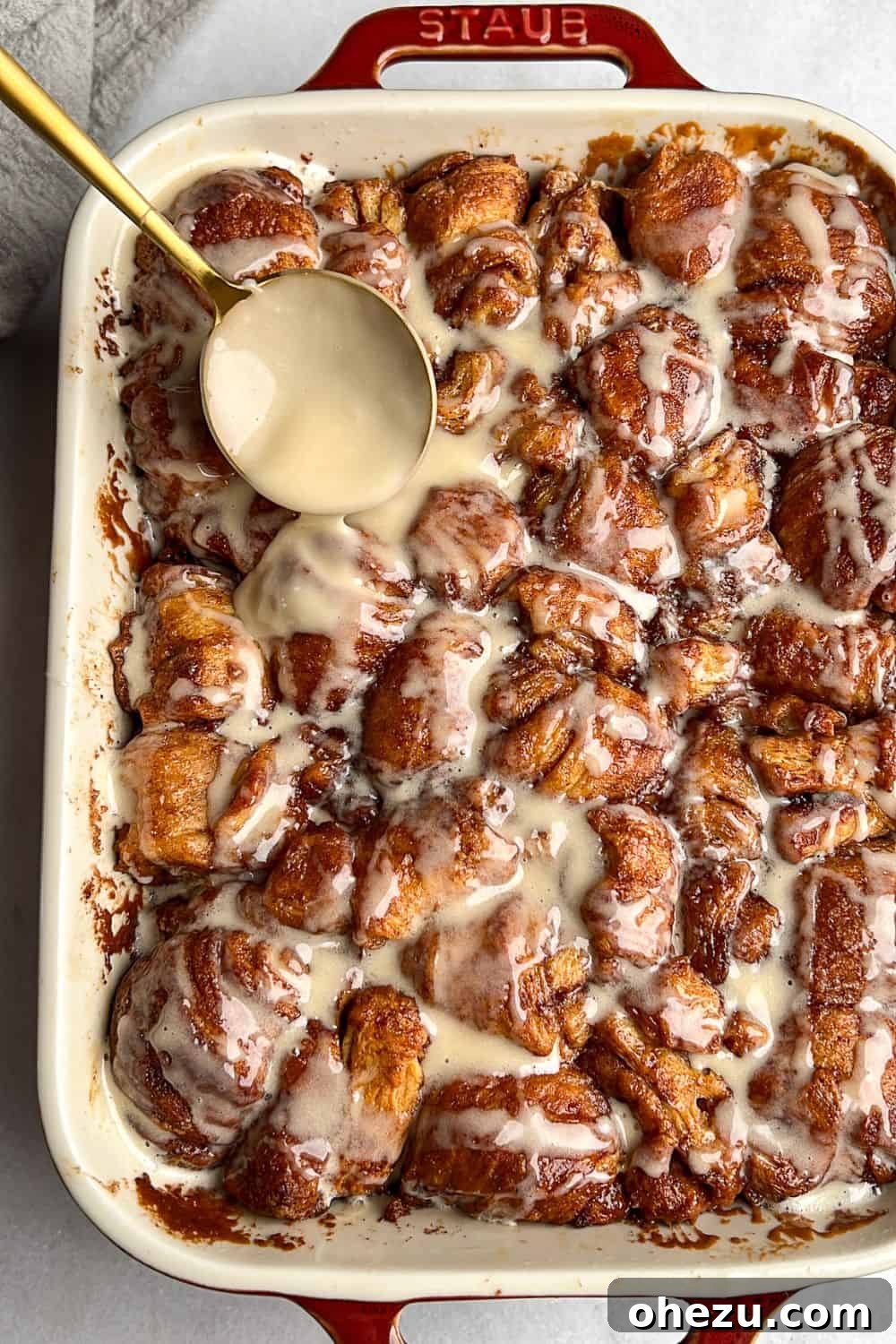 This shortcut recipe uses store-bought dough to create warm, buttery cinnamon roll bites in under an hour. You won't be able to resist! Drizzling frosting over a baking dish filled with warm, golden-brown cinnamon roll bites, highlighting their gooey centers and sweet glaze.