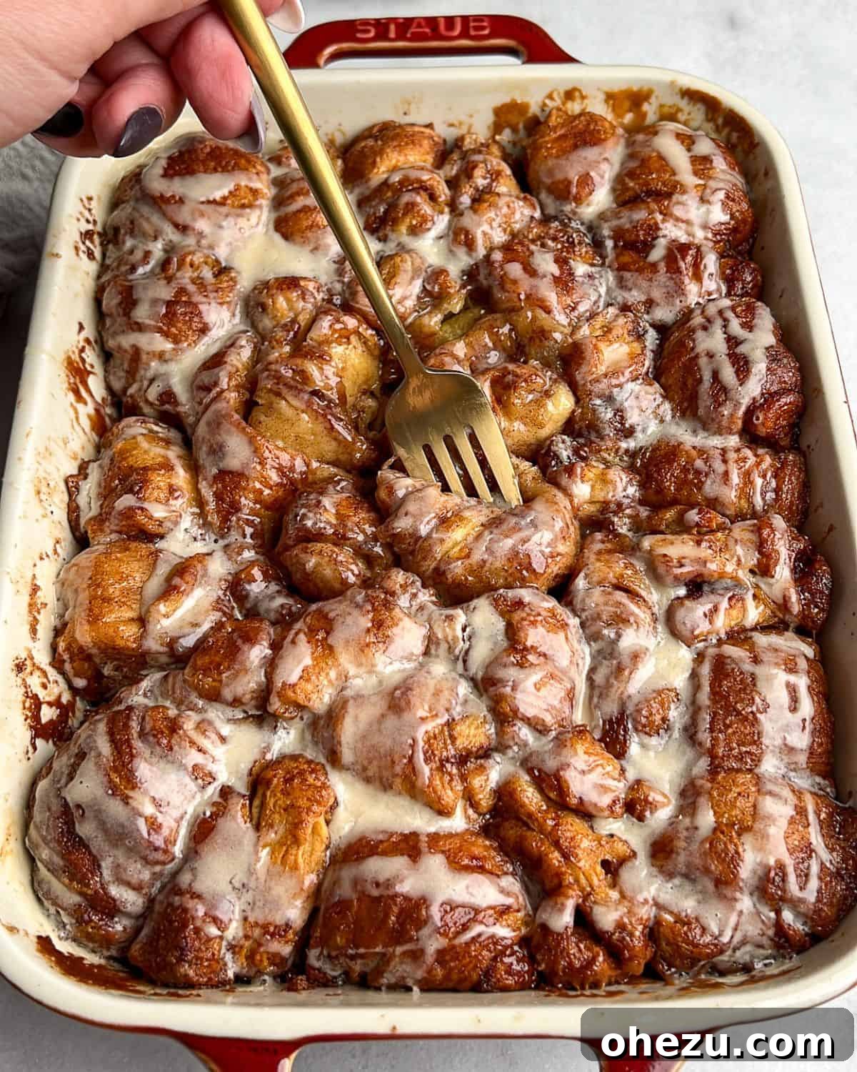 This shortcut recipe uses store-bought dough to create warm, buttery cinnamon roll bites in under an hour. You won't be able to resist! A fork taking a bite from a pan of warm, frosted cinnamon roll bites, emphasizing their soft texture and gooey center.