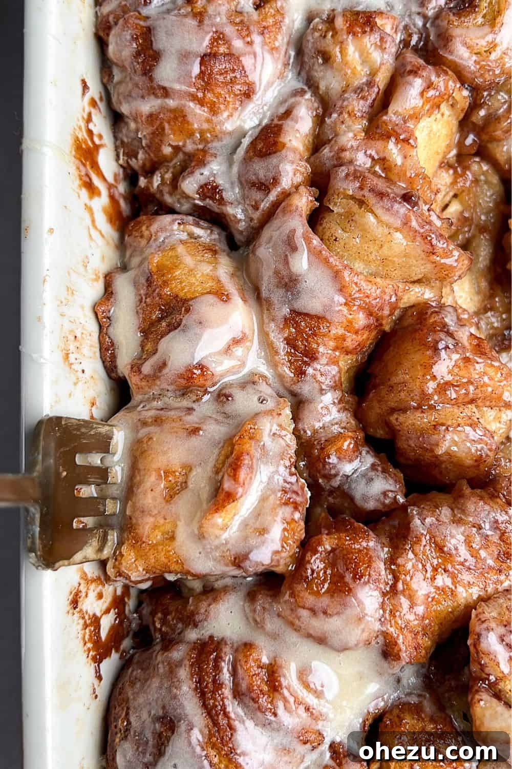 This shortcut recipe uses store-bought dough to create warm, buttery cinnamon roll bites in under an hour. You won't be able to resist! A close-up of a fork piercing a cinnamon roll bite, highlighting the deep caramelization and soft interior, nestled in a pan of other bites.