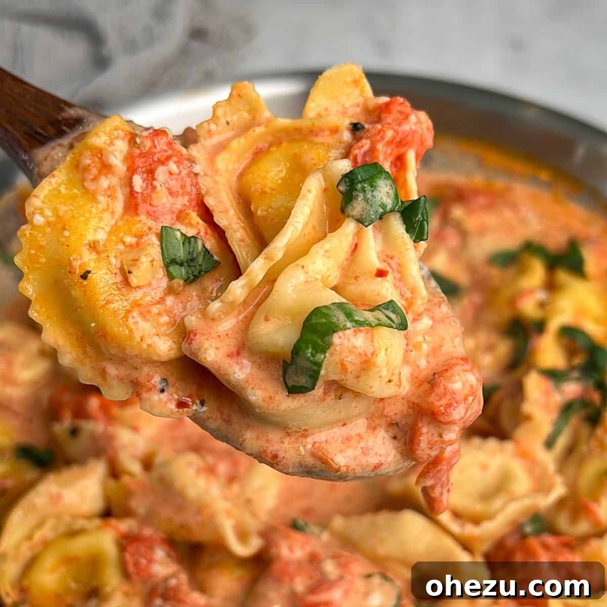 A wooden spoon holding a generous portion of creamy tomato pasta, close-up against a blurred background.