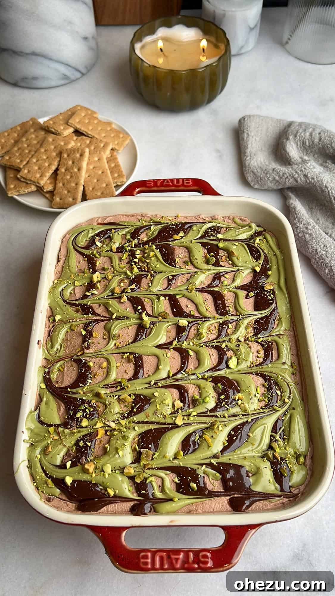 With layers of crispy kataifi, pistachio cream, and chocolate whipped cream, this Dubai chocolate cheesecake is a dream come true. Dubai chocolate cheesecake in a casserole dish near graham crackers, ready to be served.