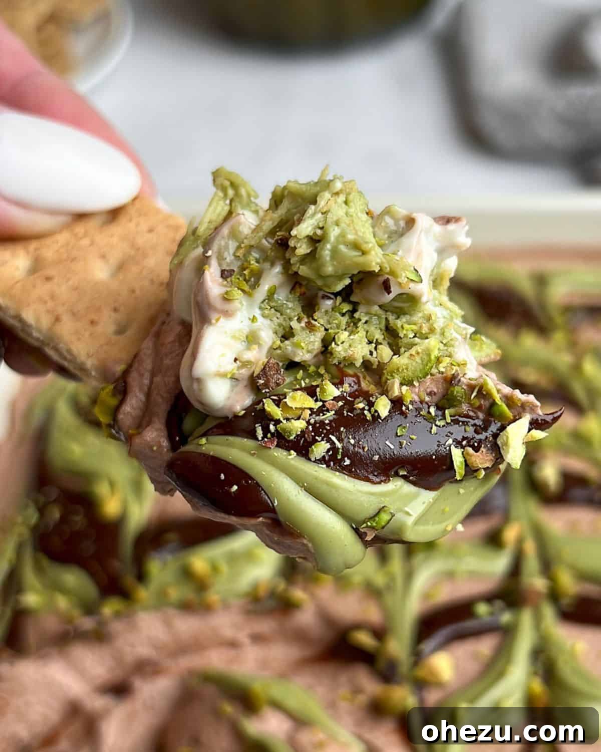 With layers of crispy kataifi, pistachio cream, and chocolate whipped cream, this Dubai chocolate cheesecake is a dream come true. A graham cracker perfectly scooping up a portion of the delicious Dubai chocolate cheesecake, highlighting its layers.