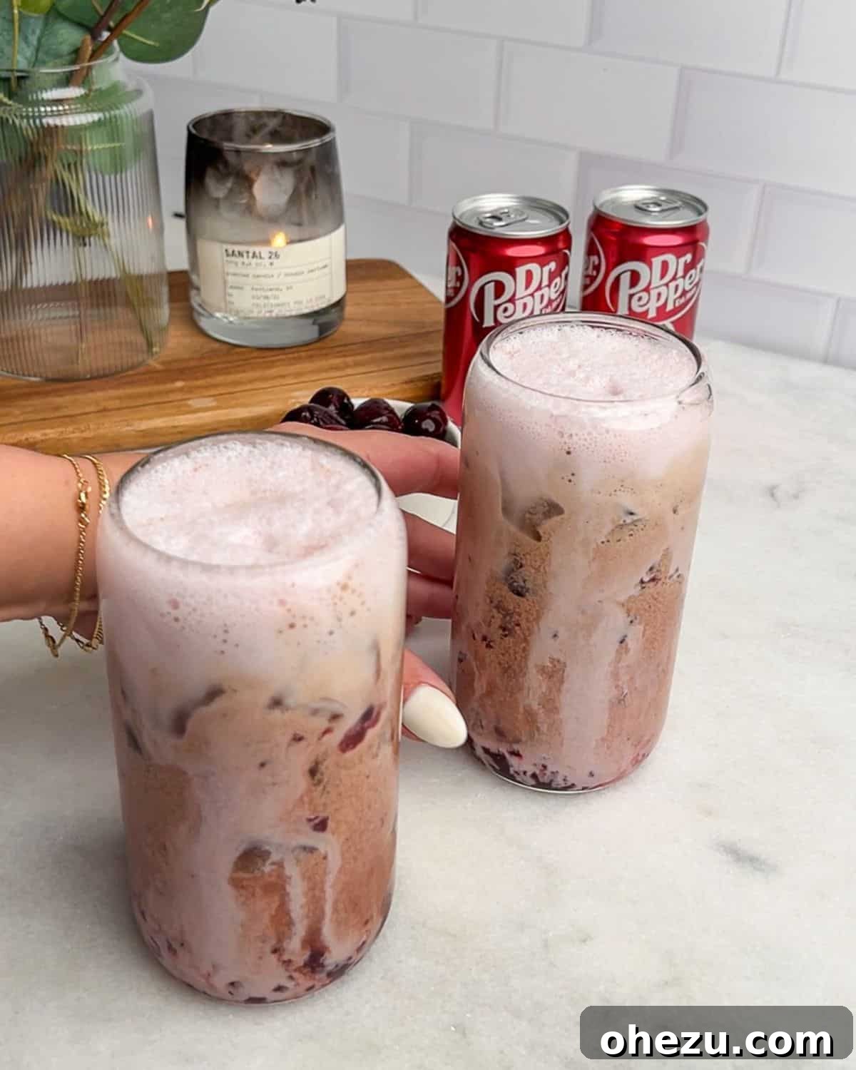 two glasses of cherry vanilla soda on a table with a hand grabbing the glass