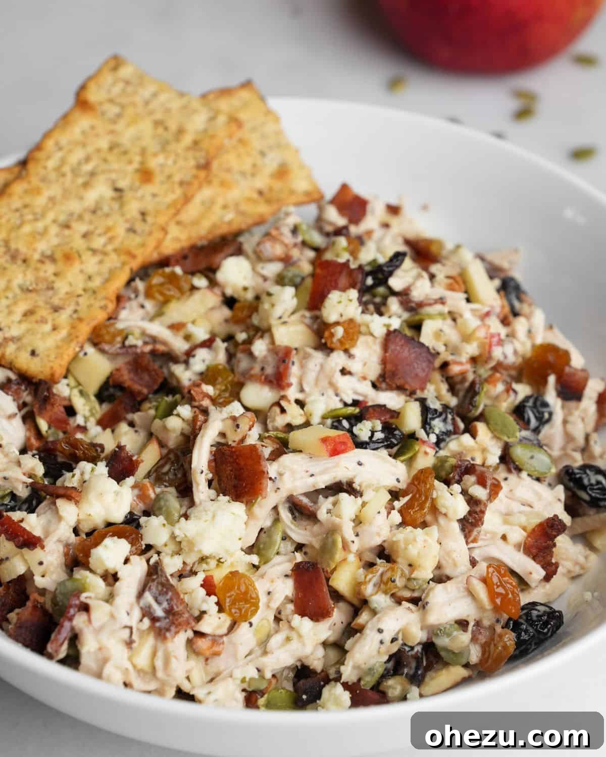 This autumn-inspired chicken salad with apples is an ideal blend of savory chicken, crisp apples, crunchy pecans, and so much more. Autumn chicken salad in a white bowl, served with an assortment of crackers on a wooden board.