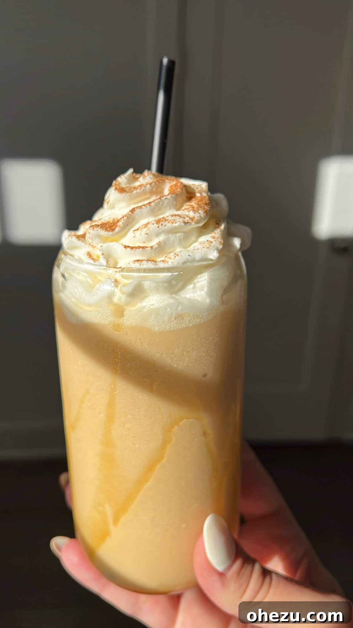A hand holding a glass of whipped caramel apple cider against the backdrop of a beautiful sunset.