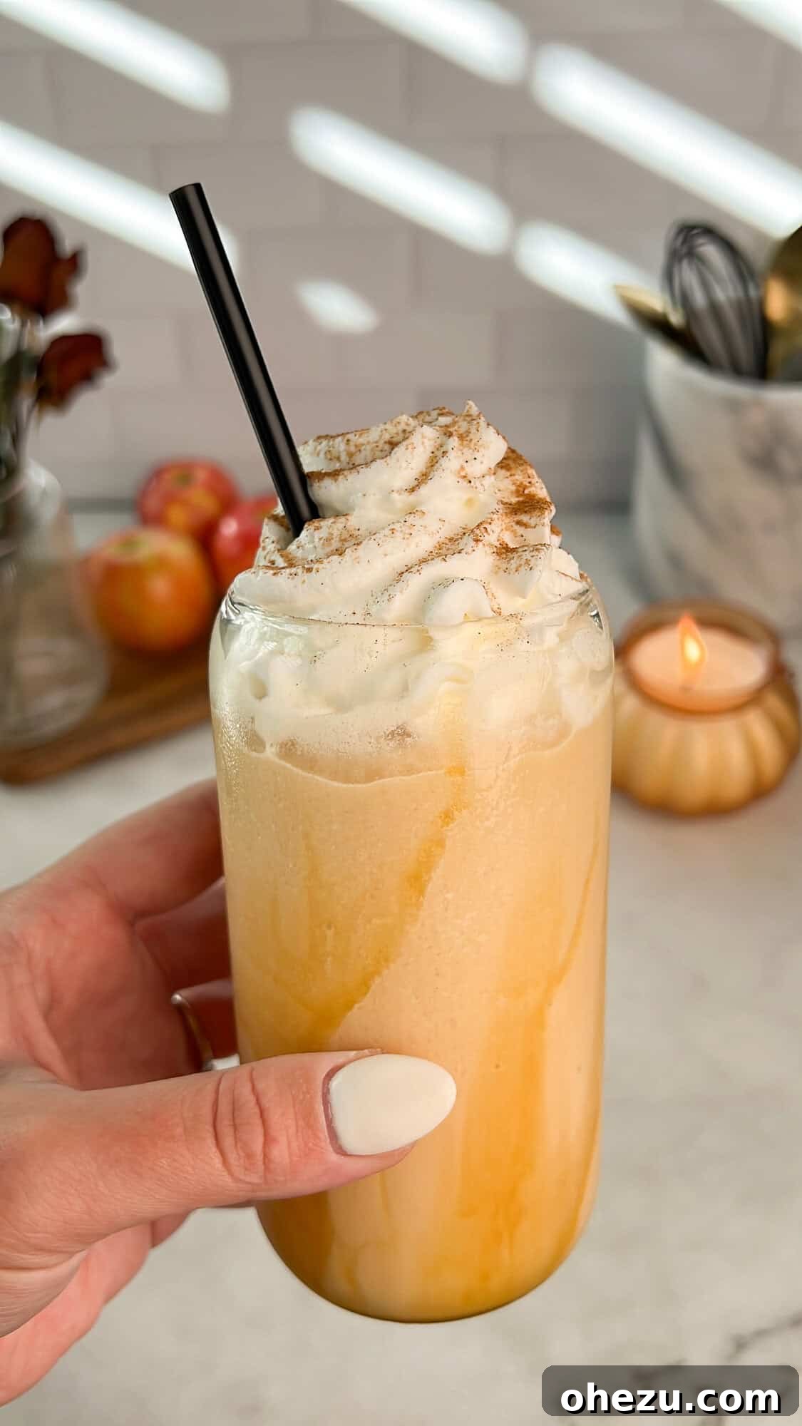 A person holding a glass of whipped caramel apple cider, highlighting the creamy texture and delicious fall appeal.