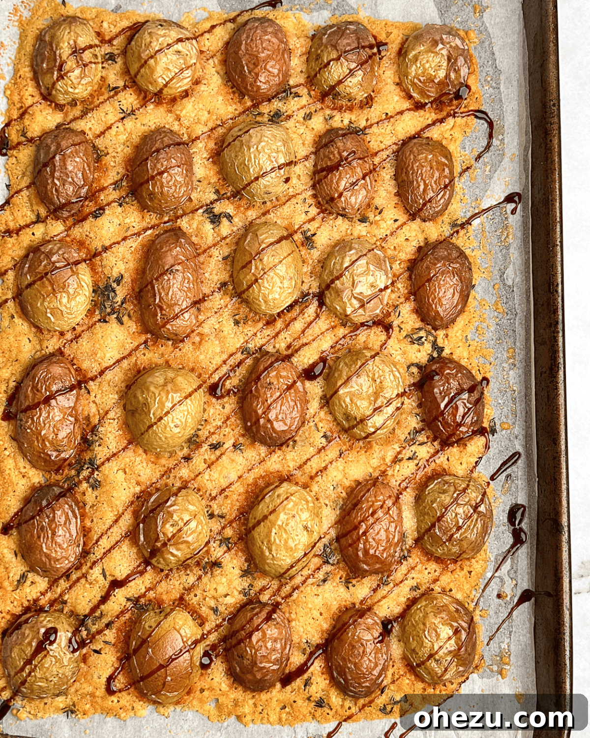 Platter of Parmesan roasted potatoes, many drizzled with balsamic glaze, highlighting their perfect golden crispness.