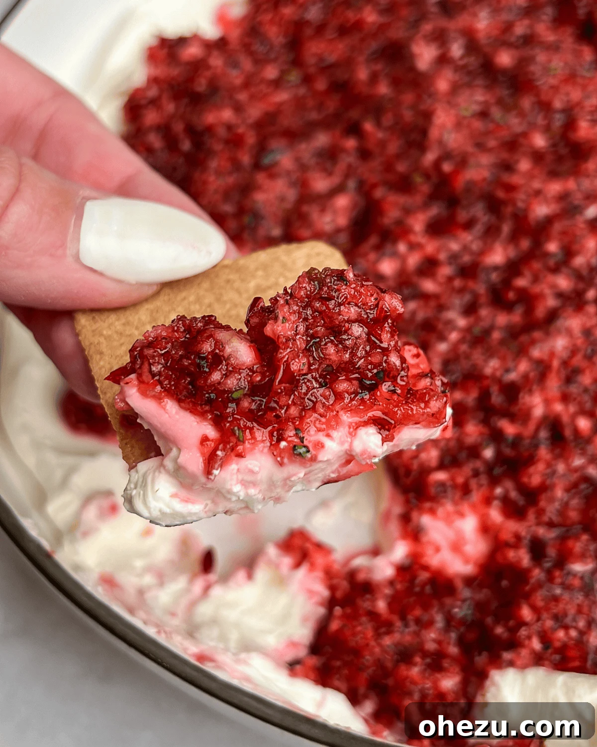 Sweet Heat Cranberry Jalapeno Dip 2 featured image for Cranberry jalapeno cream cheese dip with a hand holding a cracker