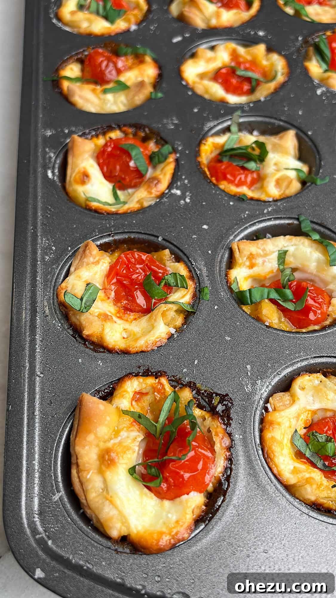 Caprese bites fresh out of the oven, still in a mini muffin tin, perfectly baked and ready for garnishing.