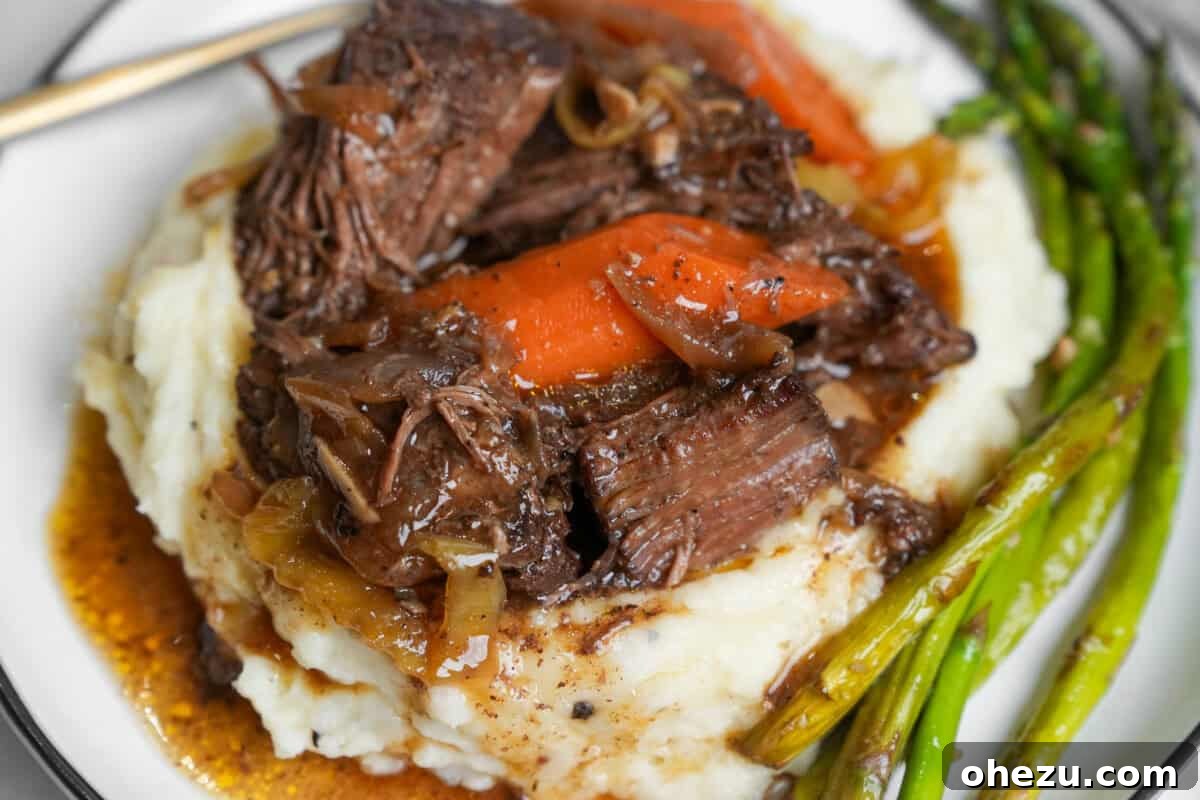 Up close image of succulent Mississippi pot roast and rich juices served over creamy mashed potatoes, ready to be enjoyed.