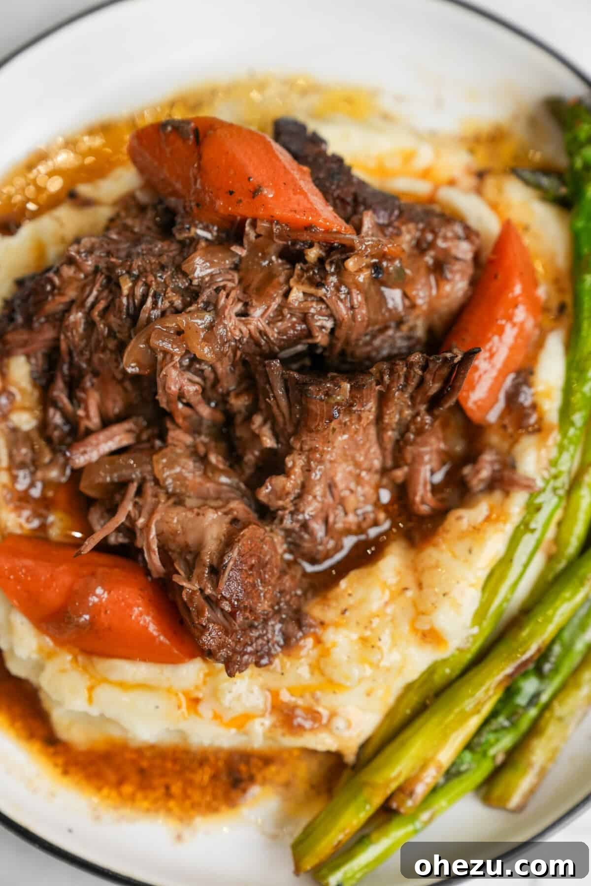Plated Mississippi pot roast, elegantly served over creamy mashed potatoes, garnished with fresh asparagus spears.