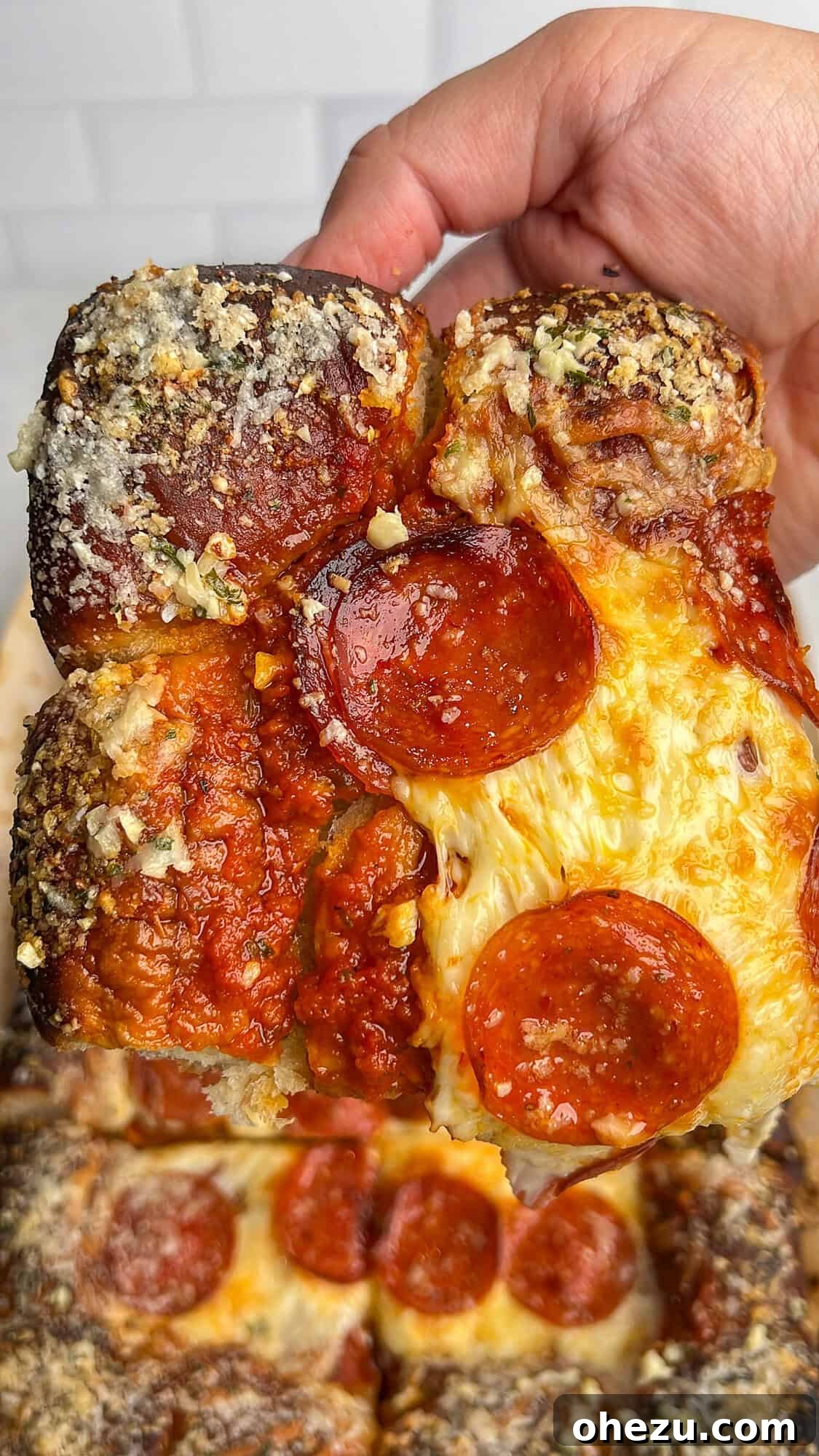 A square slice of Hawaiian roll pizza with melted cheese and crispy pepperoni, showcasing the soft crust.