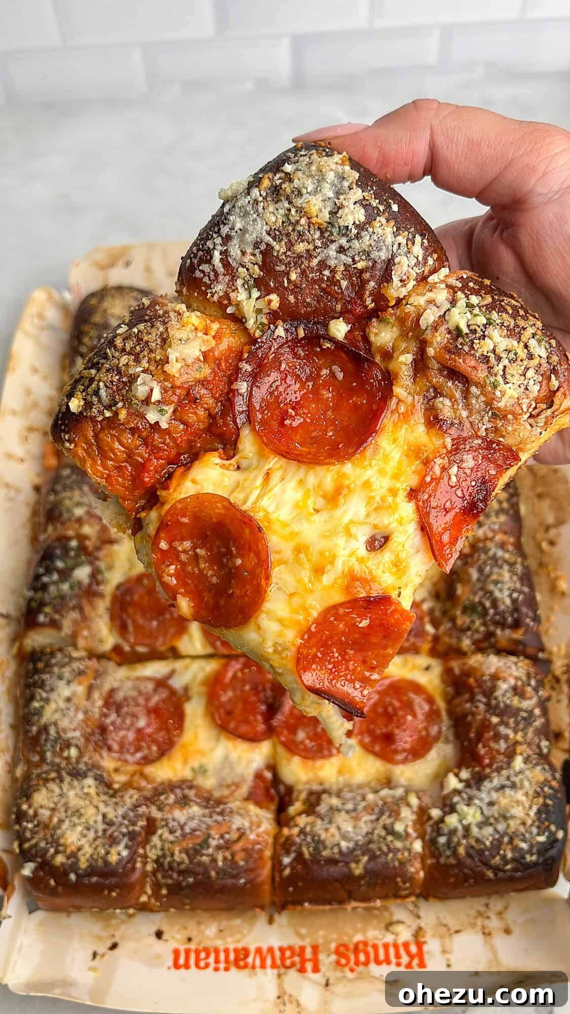 A hand holding a perfectly baked slice of Hawaiian roll pizza, showing the thick, golden crust and melted cheese.
