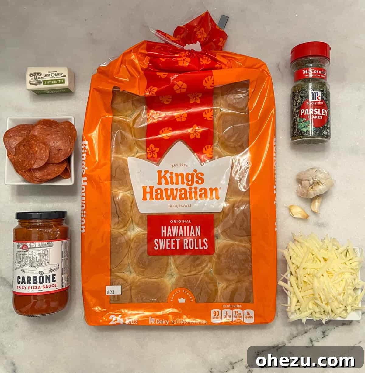 All the fresh ingredients needed for Hawaiian Roll Pizza laid out on a kitchen counter, including rolls, sauce, cheese, and butter.