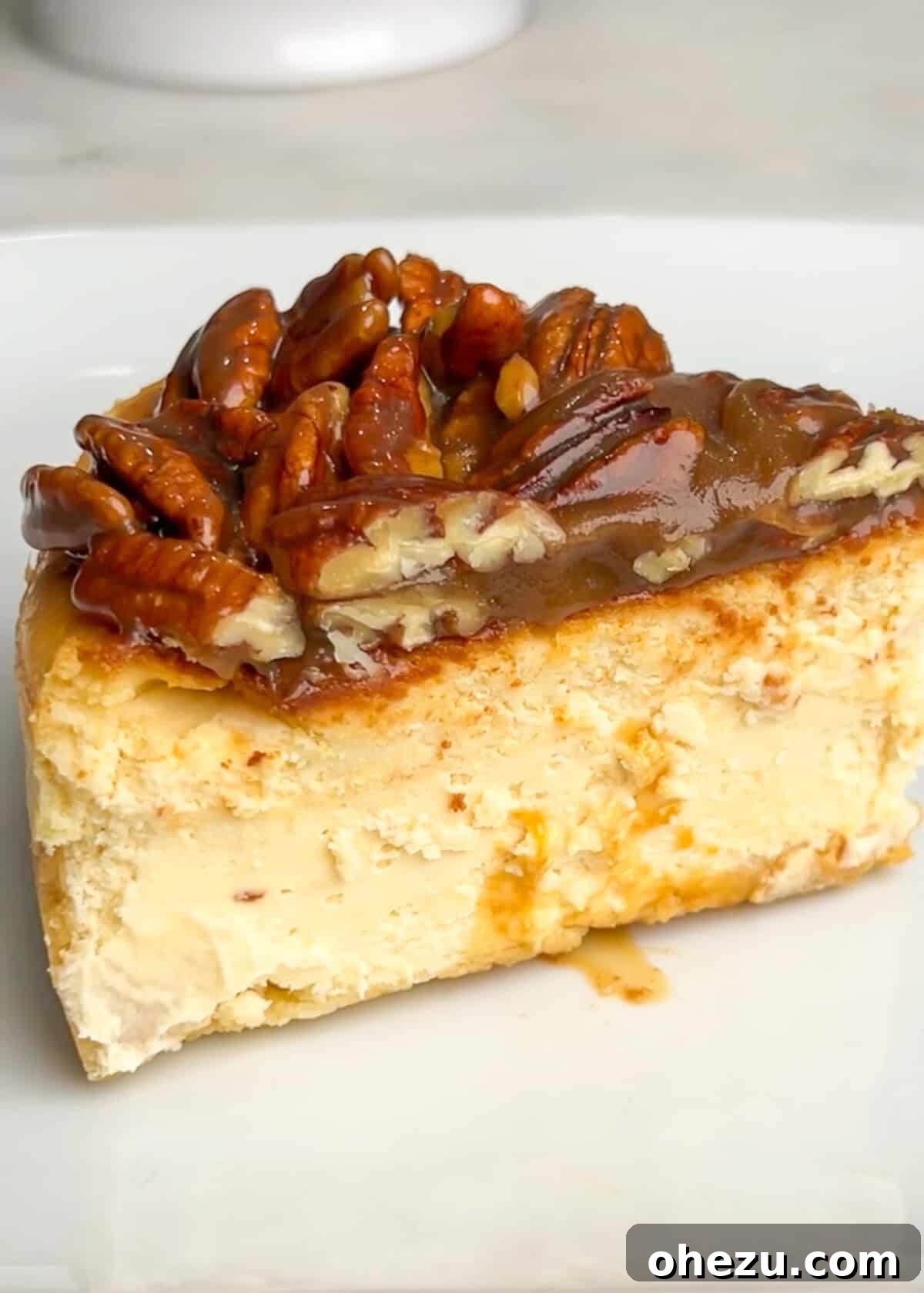 A perfect slice of Bourbon Pecan Cheesecake on a white plate, showcasing its distinct layers and creamy texture.