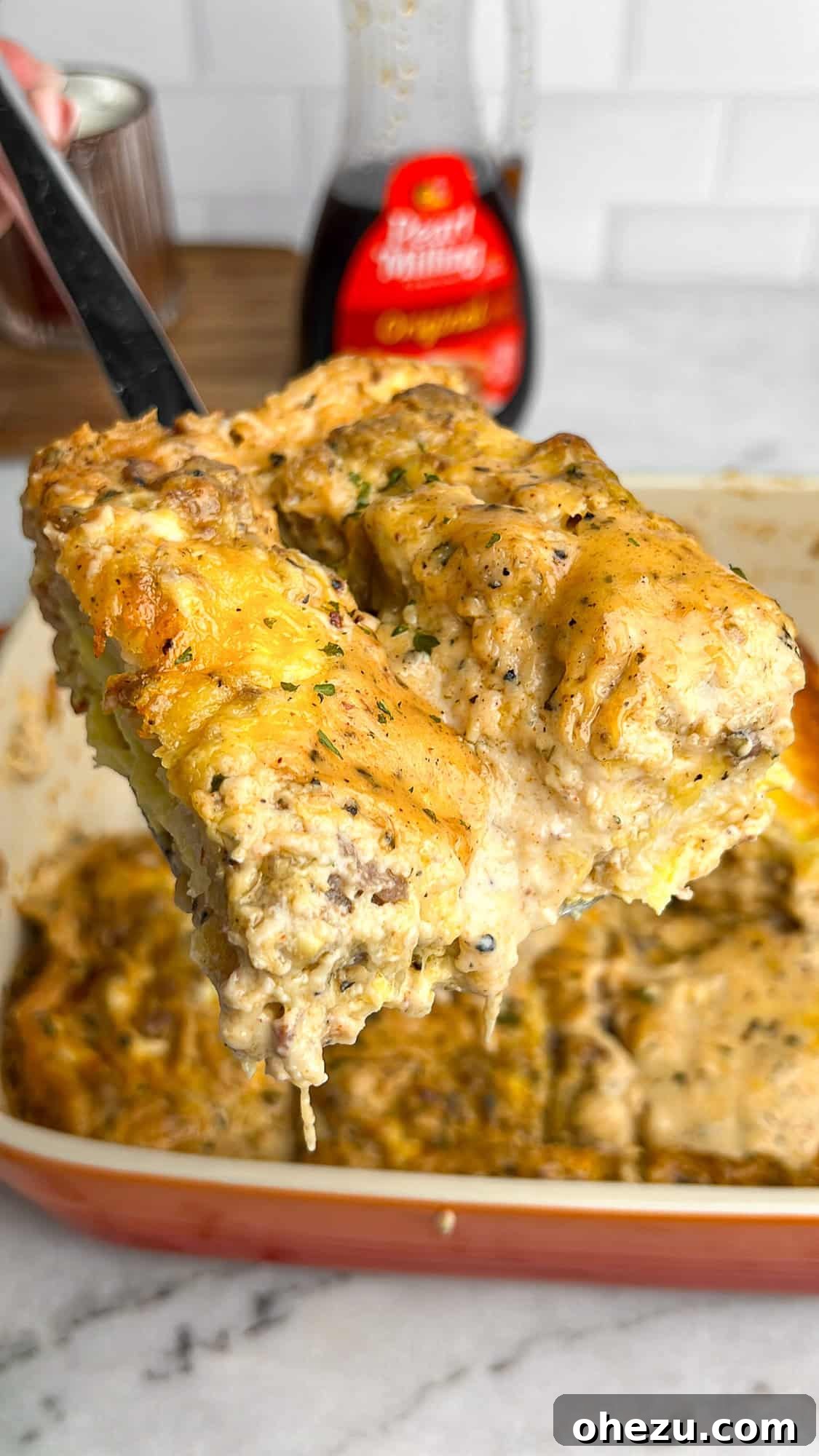 A perfectly portioned slice of golden-brown biscuits and gravy casserole, topped with fresh herbs, resting on a spatula, ready to be served from a large baking dish.
