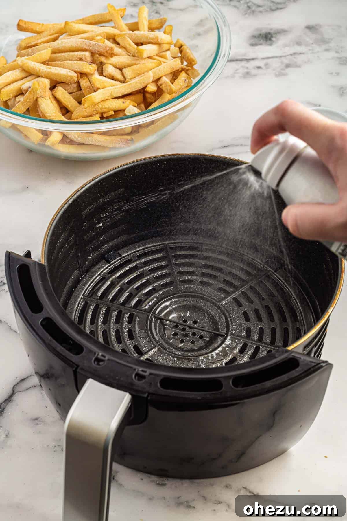 Golden Crispy Air Fryer Frozen French Fries 3 A hand gently spraying cooking oil into an empty air fryer basket, preparing it for a batch of frozen french fries.