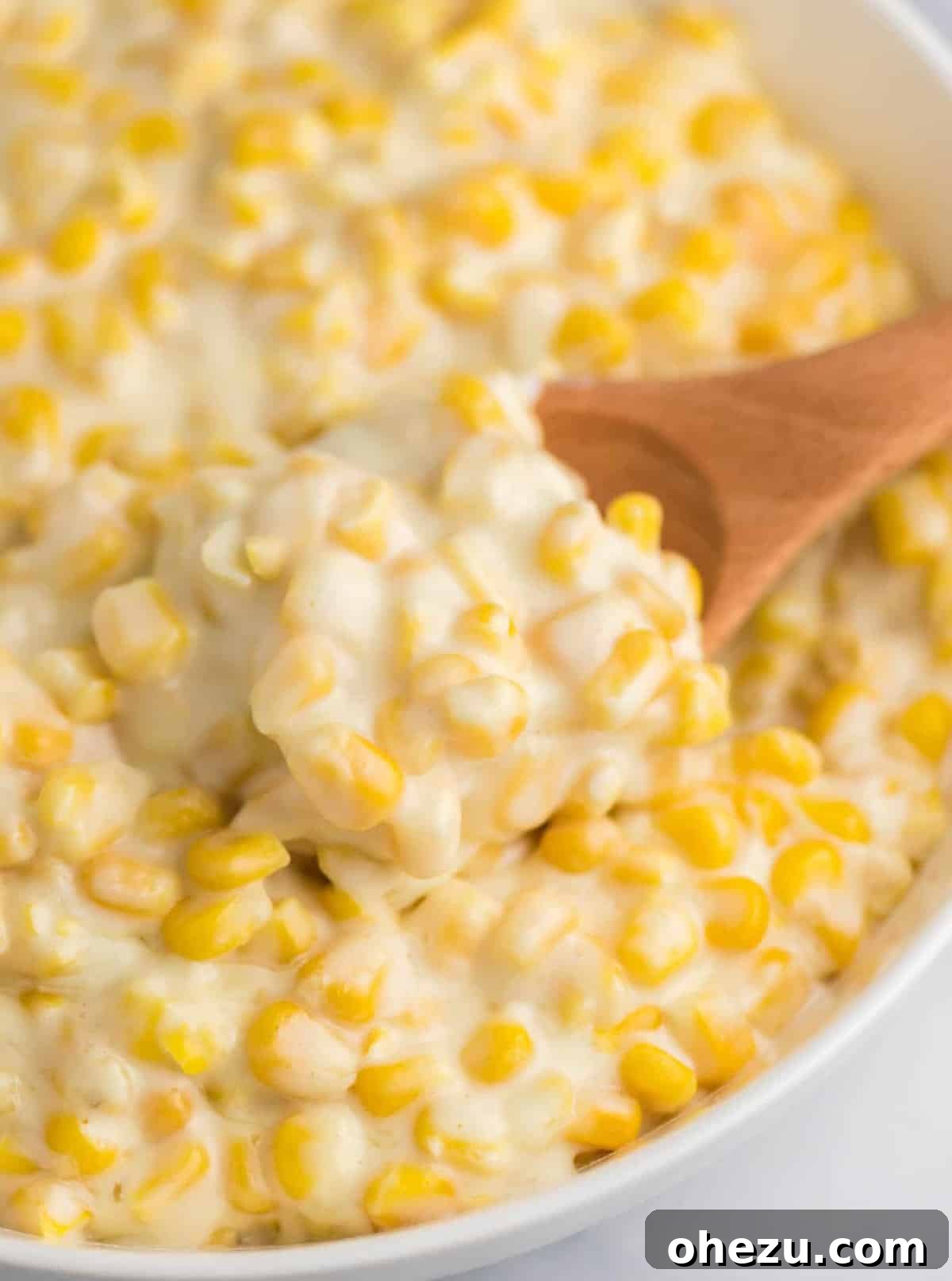 A wooden spoon taking a scoop of creamy, golden creamed corn from a serving dish, highlighting its luscious texture.