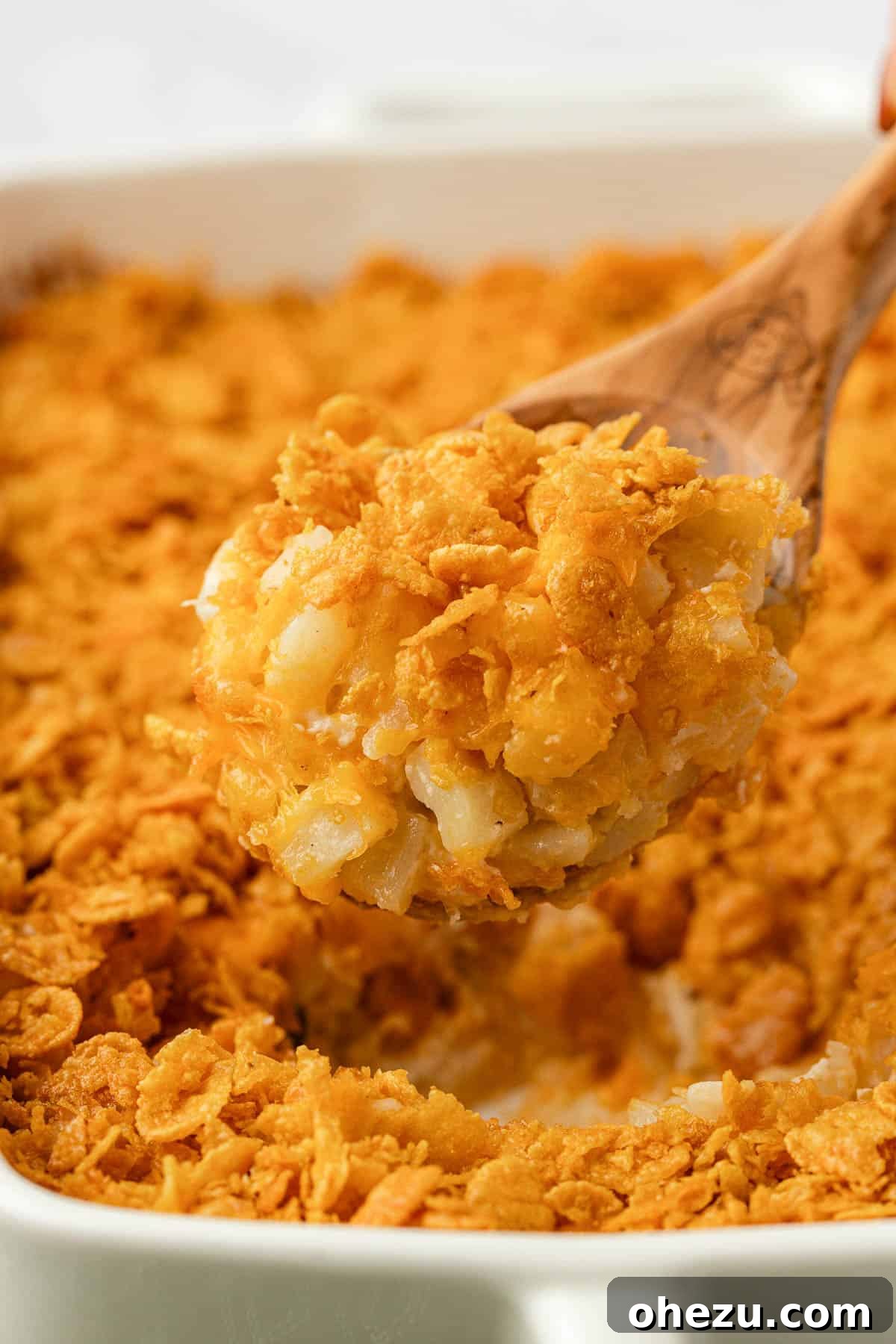 Scooping a serving of golden, bubbly funeral potatoes from a baking dish