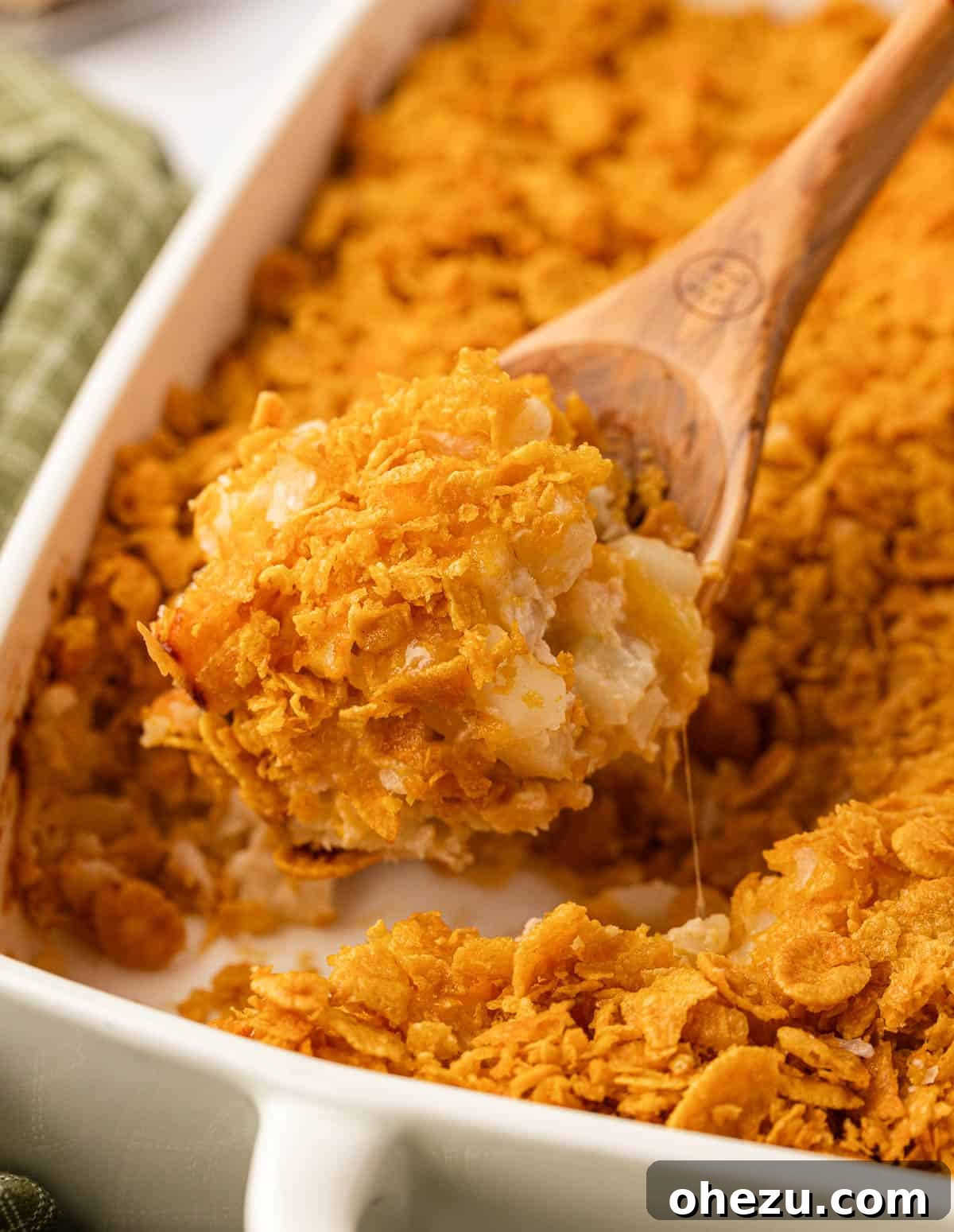 A scoop of delicious funeral potatoes being lifted from the casserole dish, showing steam and texture