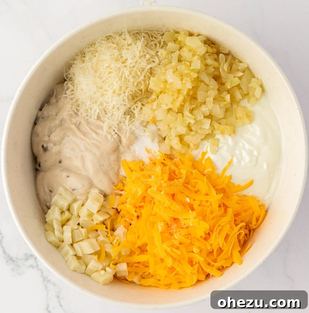 All funeral potato ingredients, including thawed hash browns, soup, and cheese, in a large mixing bowl