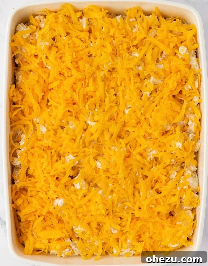 Cheesy hash brown potatoes in a baking dish topped with a final layer of shredded cheddar cheese