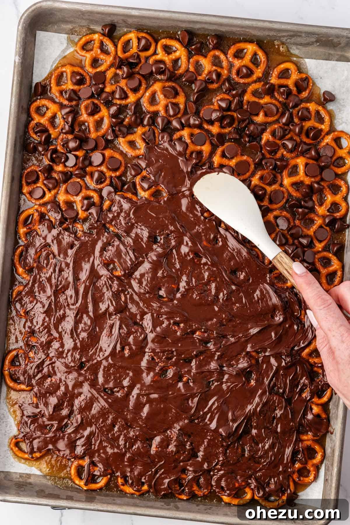 spreading the melted chocolate over the pretzels with a rubber spatula
