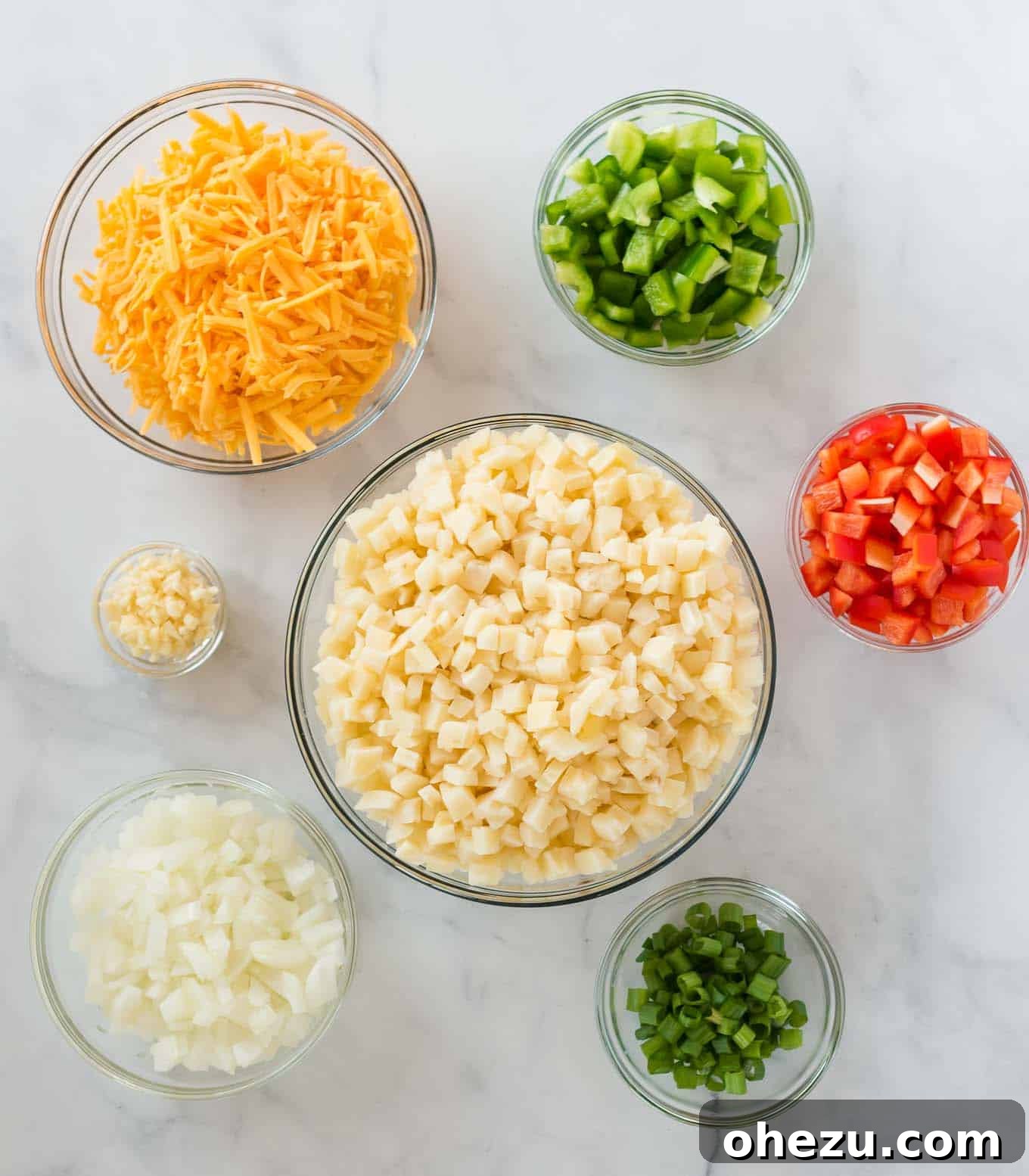 Sunrise Hash Brown Egg Bake 3 Separate glass bowls displaying the fresh ingredients: thawed cubed hash browns, minced garlic, diced yellow onion, colorful bell peppers, grated sharp cheddar cheese, and chopped green onions.