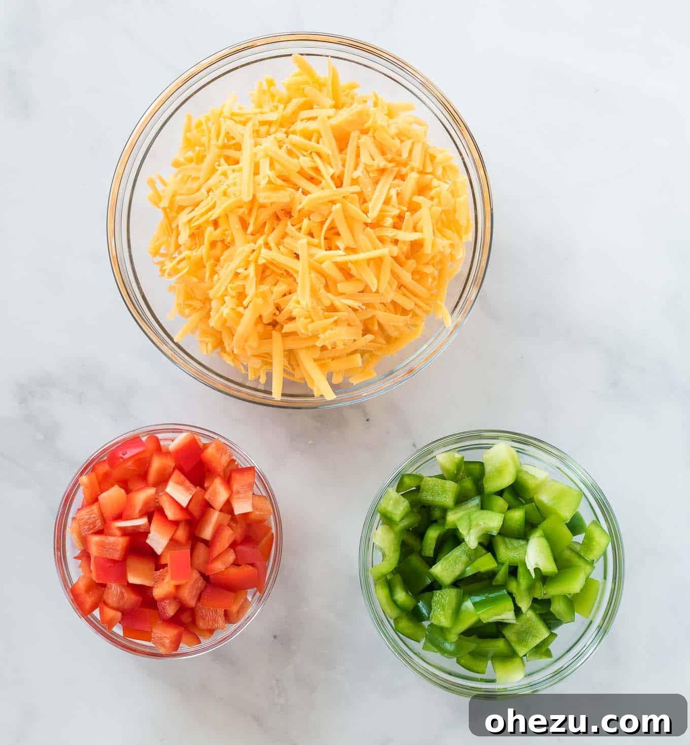 Sunrise Hash Brown Egg Bake 4 Separate glass bowls holding freshly grated sharp cheddar cheese, diced red bell pepper, and diced green bell pepper.