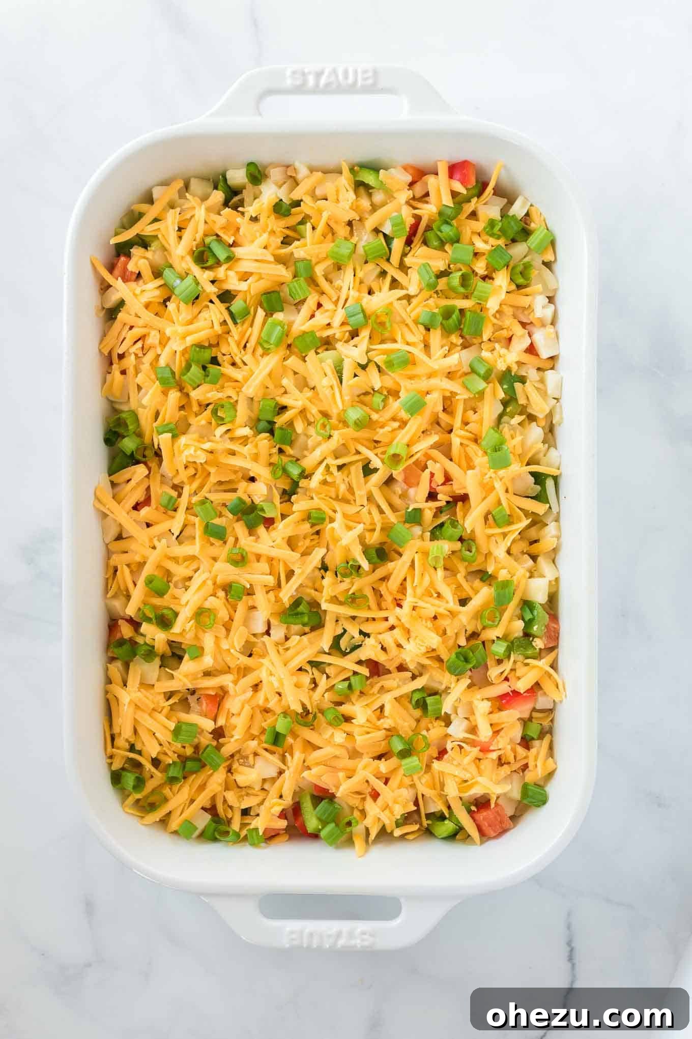 Sunrise Hash Brown Egg Bake 8 The casserole topped with a generous layer of sharp cheddar cheese and vibrant green onions, ready for baking.