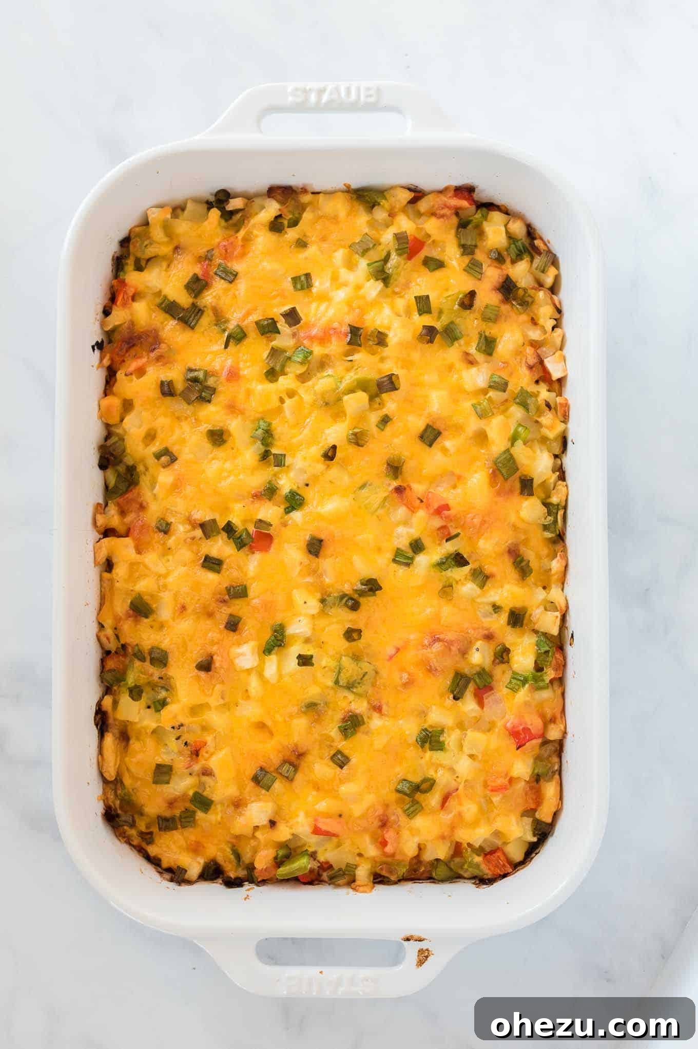 Sunrise Hash Brown Egg Bake 9 The finished baked hash brown egg casserole, golden brown and bubbly, resting in a white baking dish on a wooden surface.