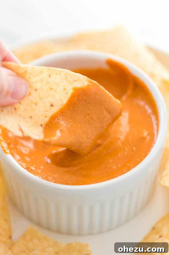 Crispy tortilla chip perfectly dipped into a bowl of creamy, golden vegan queso