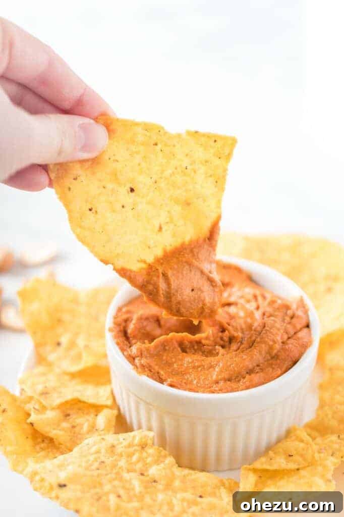 Another image of a chip dipped in a white ramekin of smooth vegan queso