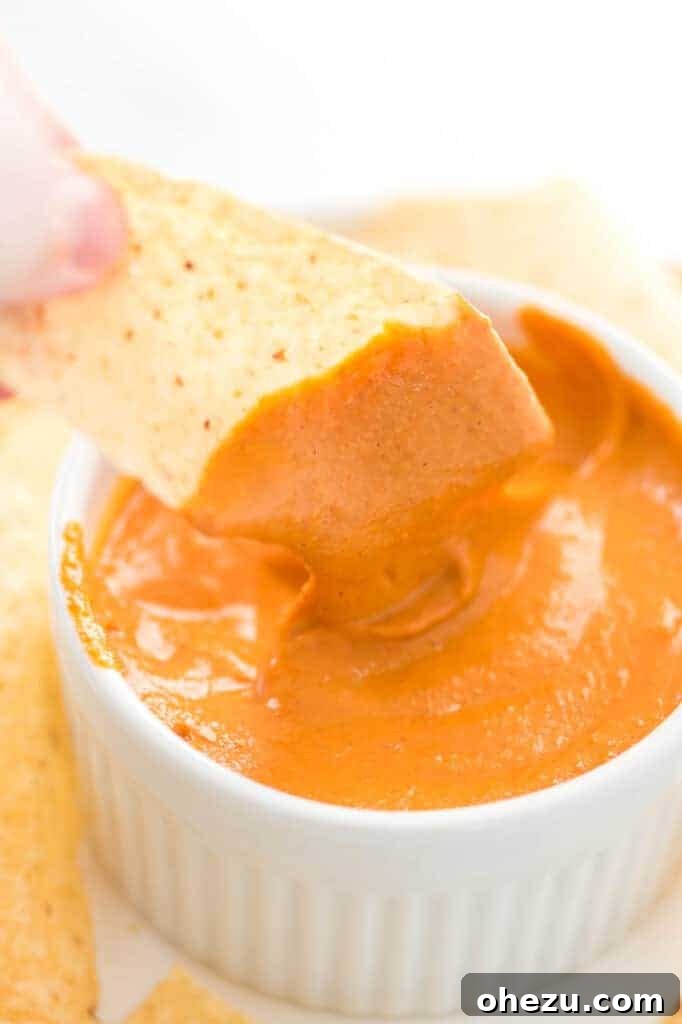 A chip half-dipped into vegan queso, showcasing the rich color and inviting texture
