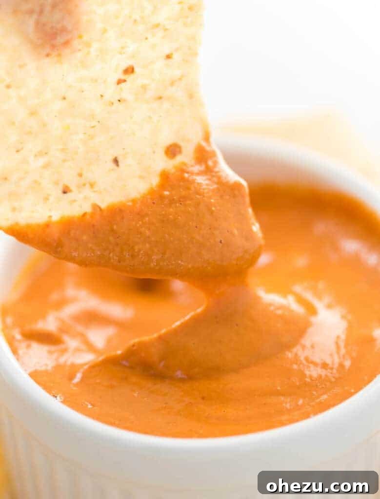 A second close-up shot of a chip submerged in smooth vegan queso, highlighting its creamy texture