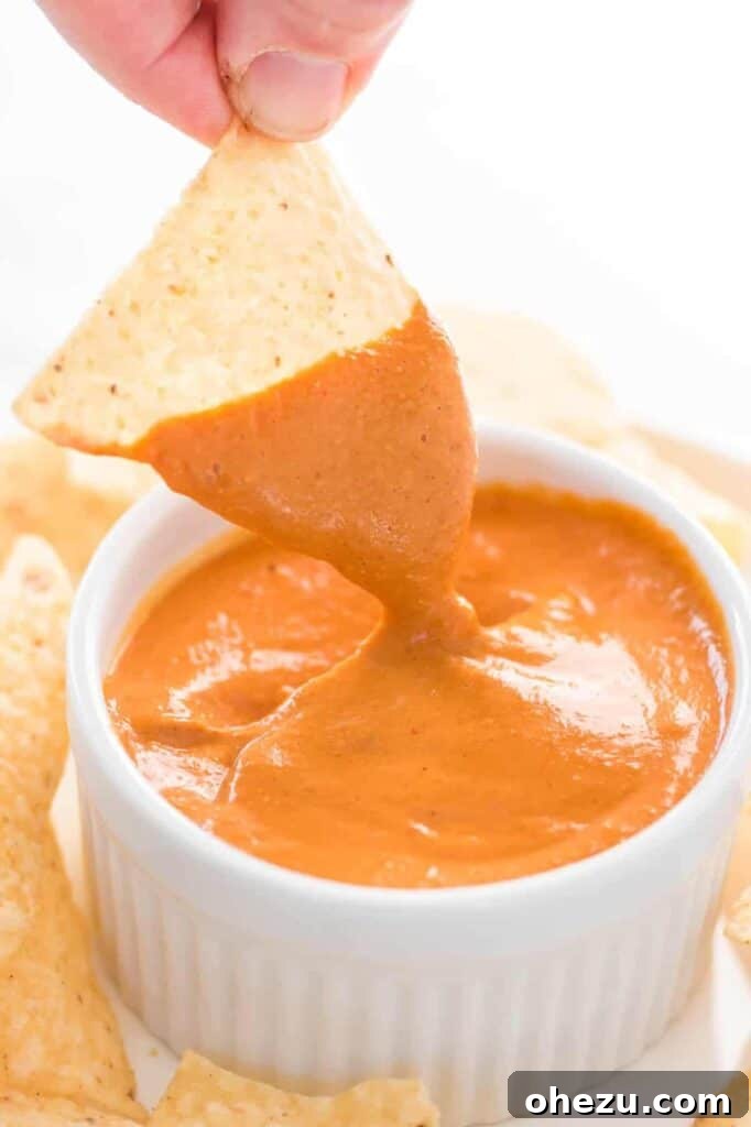 A tortilla chip being dipped into a small white ramekin filled with delicious vegan queso