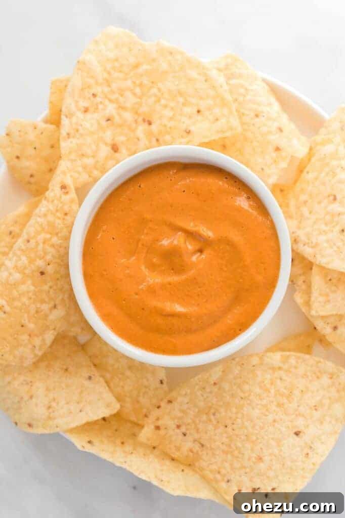 A white ramekin of vegan queso surrounded by a generous amount of tortilla chips, ready for dipping