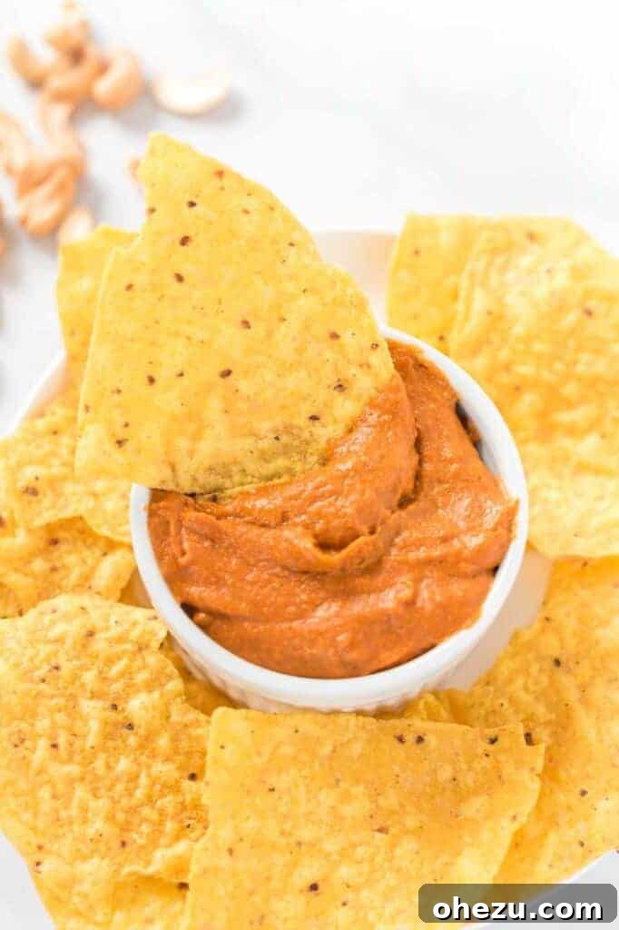 A single chip dipped into a white ramekin of rich vegan queso
