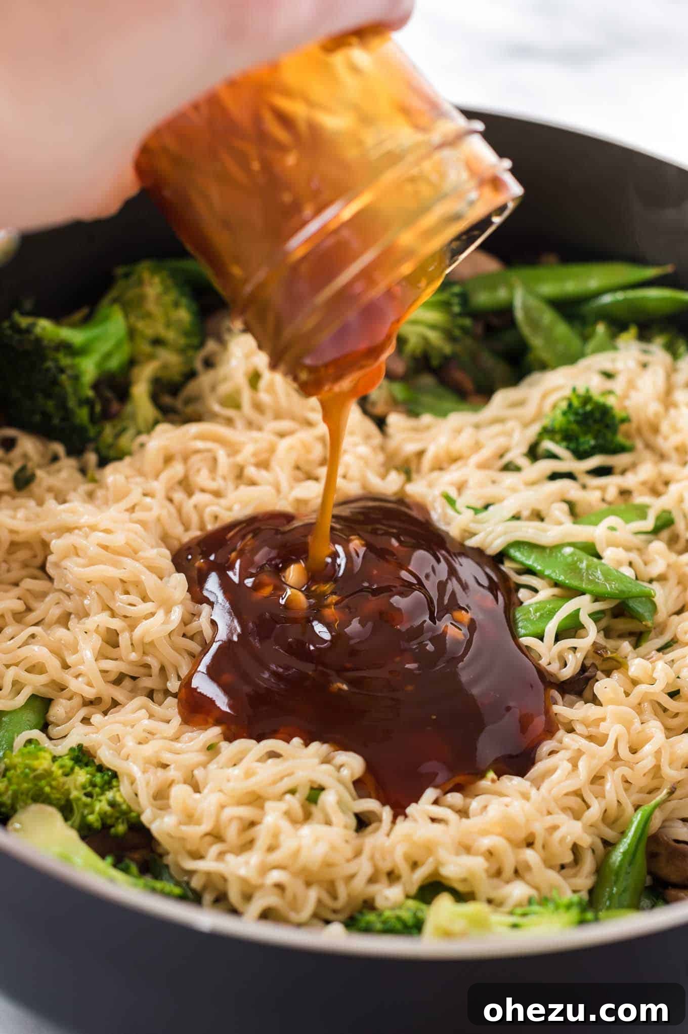 Sweet and Savory Teriyaki Noodles 5 Sweet and savory homemade teriyaki sauce being poured over sautéed vegetables and ramen noodles in a skillet.