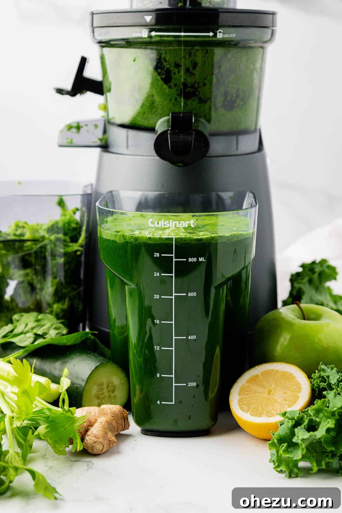 Vibrant Green Goodness 3 A glass of green juice sits next to a juicer, with fresh ingredients visible in the background, highlighting the preparation process.