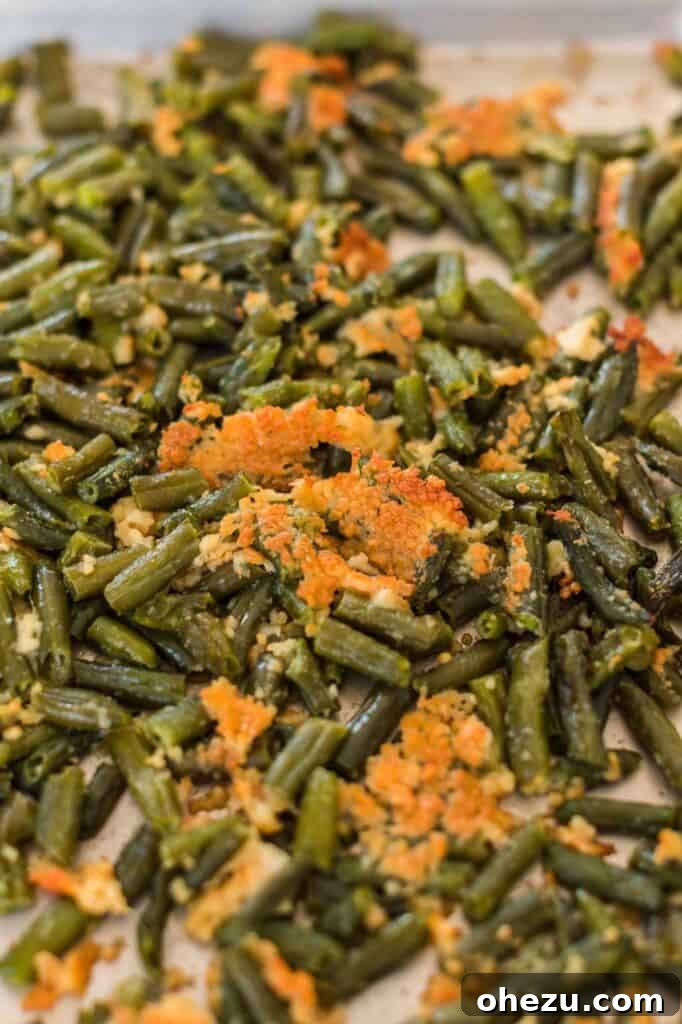 Close-up of frozen green beans tossed with olive oil and spices on a baking sheet