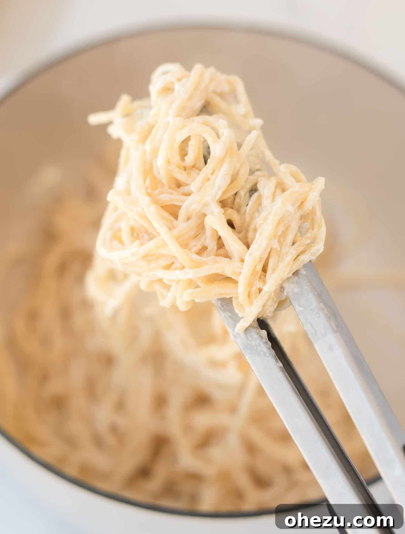 Close-up of cream cheese spaghetti noodles being tossed in a pan