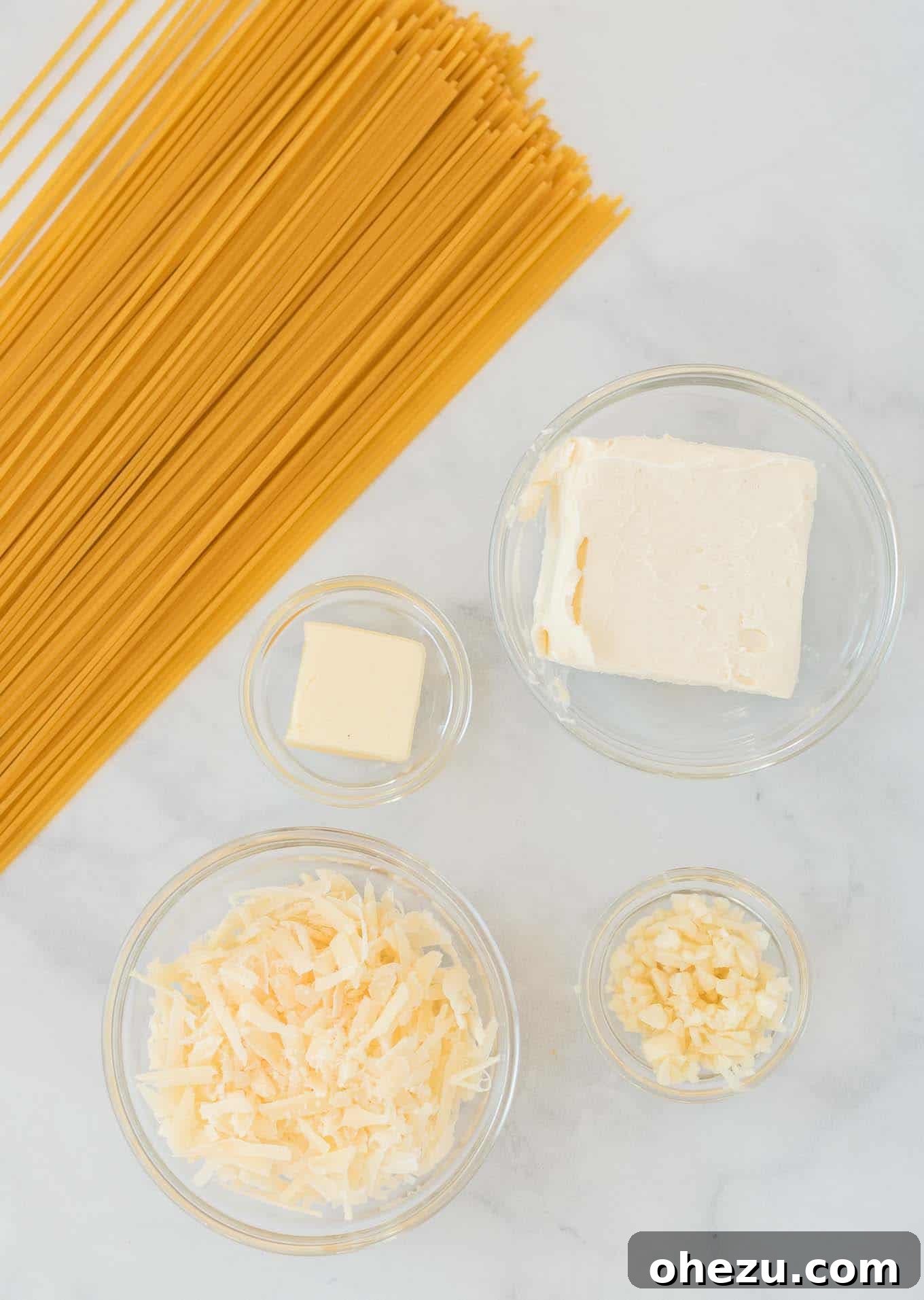 Ingredients for cream cheese pasta laid out: spaghetti, butter, garlic, cream cheese, and parmesan